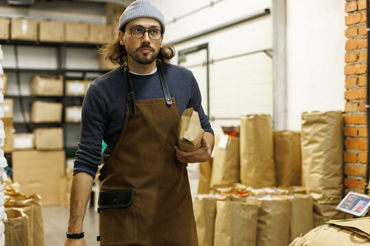 Young male worker carrying package with coffee beans at warehouse