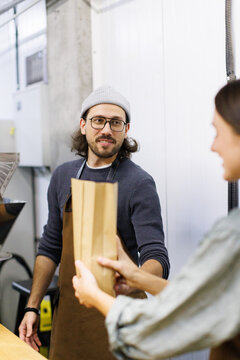 Male worker give package with coffee beans to cropped female colleague
