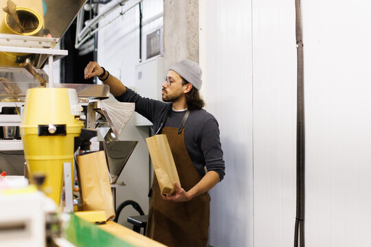 Worker with package pouring coffee beans in industrial packing machine