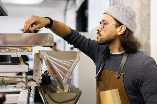 Worker with package pouring coffee beans into packing machine
