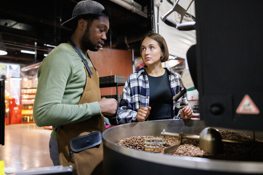 Young workers checking degree of roast in industrial roaster machine