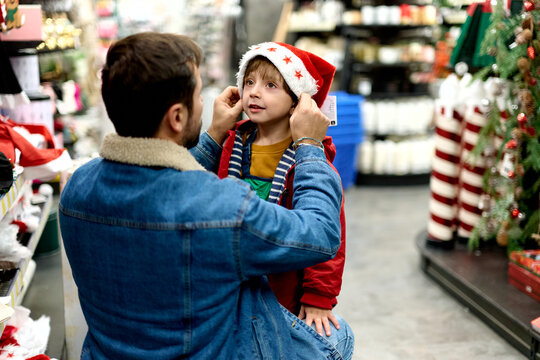 Father Helping Son Try On Santa Hat in Christmas Store