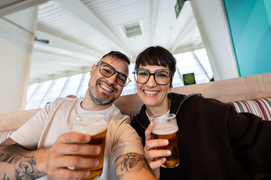Happy couple toasting beer glasses at airport bar