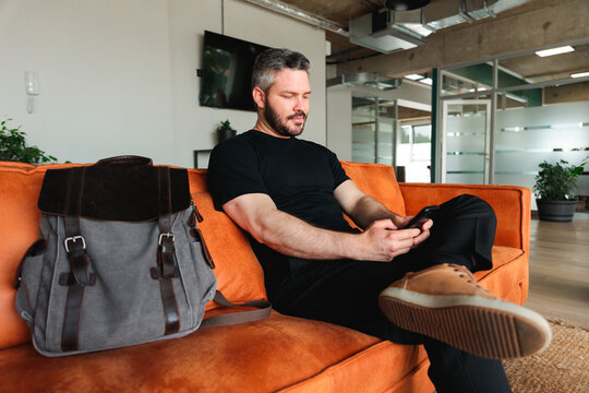 Man Checking Phone While Waiting in Coworking Lounge