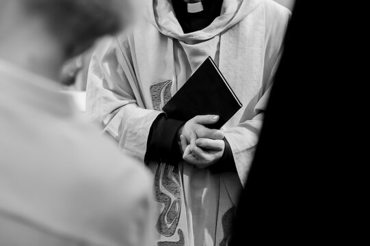 Black and white close-up of a Christian priest holding a prayer book during a church ceremony, symbolizing faith, spirituality, tradition, and solemn religious ritual.