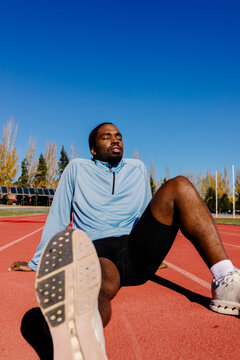 Sprinter seated on the sunlit track, taking a break and recovering