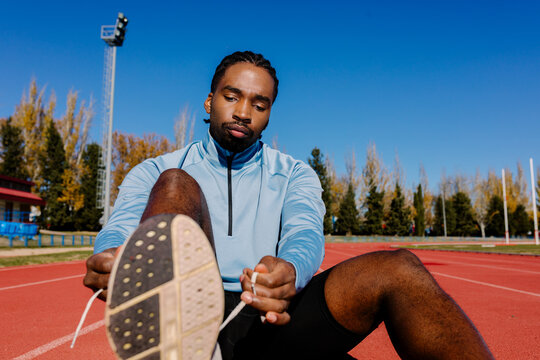 Experienced athlete sitting on the track securing his running shoes