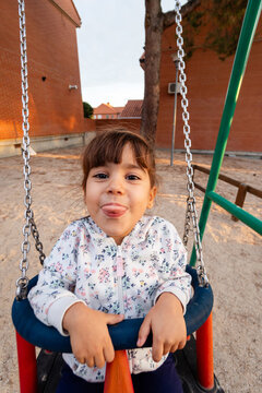 Happy child sticking tongue out on playground swing