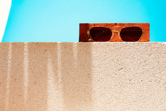 Sunglasses on a concrete block with a brick on blue background