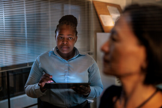 Woman with tablet in office, another woman blurred.