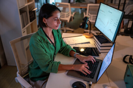 Woman analyzes data on laptop and monitor in office.