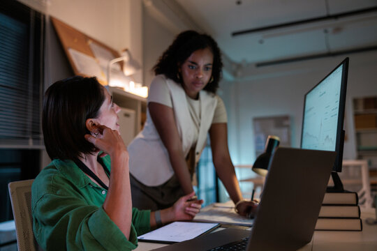Two women collaborate on data analysis in office.