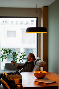 Man sits in modern room with plants and light fixture above
