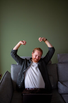 Person stretching on a couch while using a laptop at home
