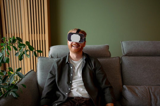 Man wearing virtual reality headset while sitting on a couch at home
