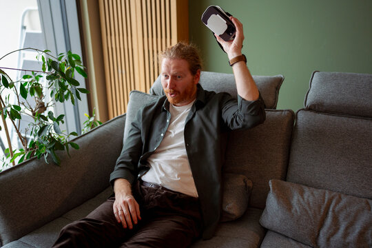 Man plays video game indoors on a couch during day
