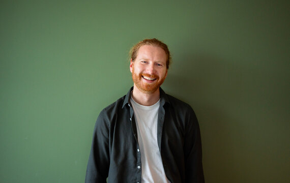 Man smiles while standing against a green wall indoors
