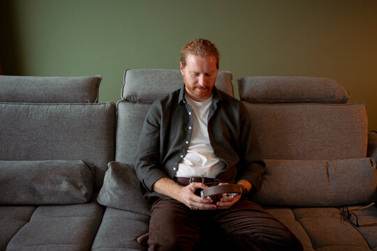 Man sitting on couch holding device in living room
