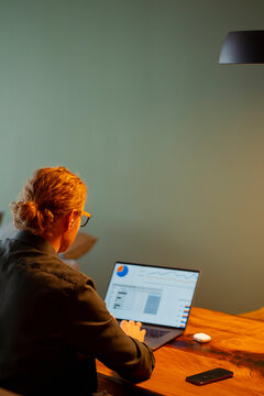 Person working on laptop at wooden table in quiet room
