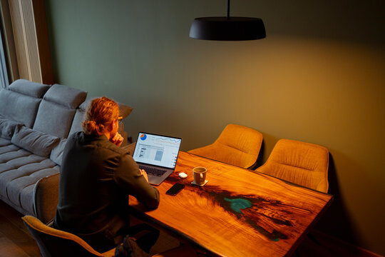 Person works on laptop at wooden table in modern room during evening
