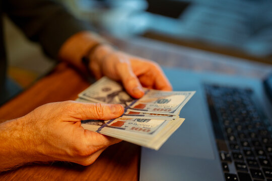 Counting cash at a desk near a laptop during evening
