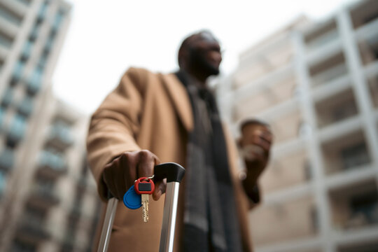 Traveler holds keys and coffee near apartment
