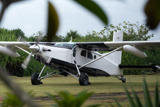 Light utility aircraft on grass airstrip in tropical setting 