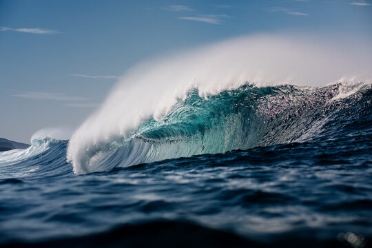 A towering wave breaking in the open sea under bright sunlight