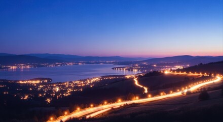 Cityscape at Night with Illuminated Winding Road and Lake Under Twilight Sky, Scenic Evening View