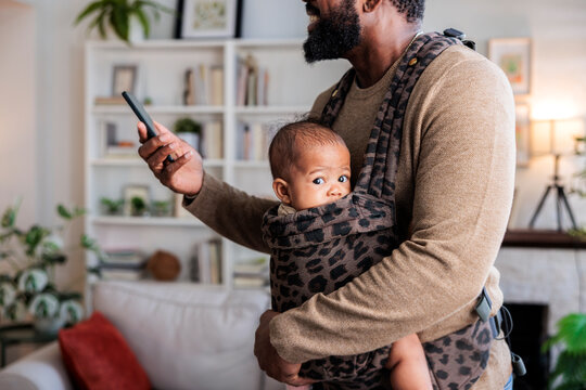 Dad with baby carrier using phone at home.