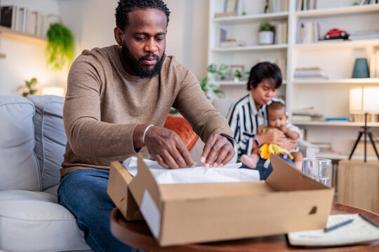 Man opens package while family watches in the background.