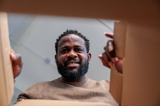 Man smiles while opening a cardboard box.