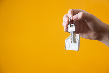 Hand holding silver keys with house shaped keychain on yellow background, concept of real estate...