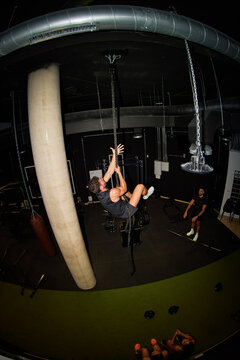 Man climbs rope in gym during training session in evening