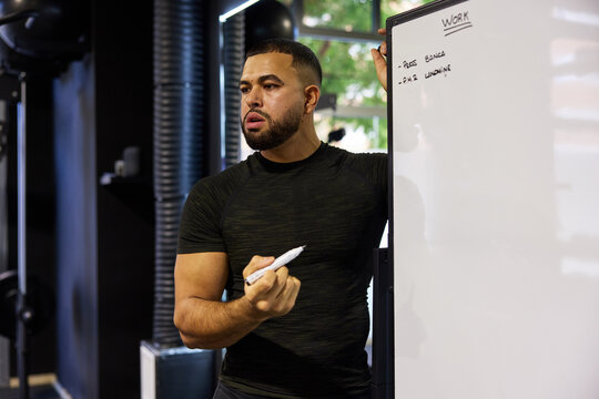 Man gives a workout lesson at a gym while using a whiteboard
