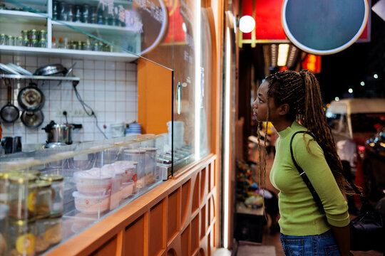 Woman gazes into a shop window at night.