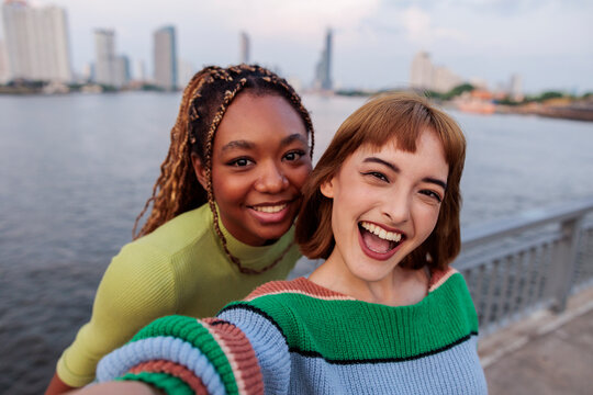 Two smiling women take a selfie with city backdrop.