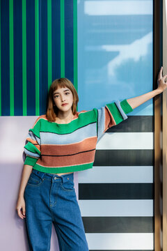 Woman in striped sweater poses against colorful wall.