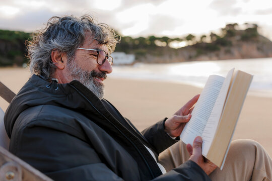 Mature man enjoying a book on beach chair