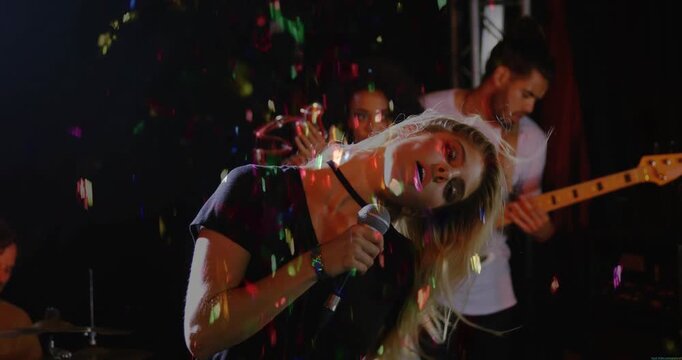 Camera rising, singer gripping mic, singing, whipping hair, scattering confetti, performing music