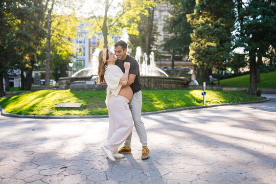 Happy pregnant couple embracing outdoors in a city park