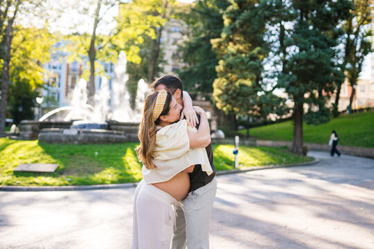 Pregnant couple embracing in city park during sunny day