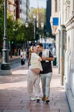 Pregnant woman and partner showing affection walking urban street