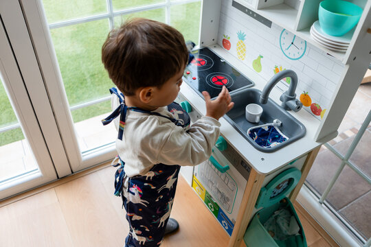 Toddler playing in toy kitchen wearing unicorn apron