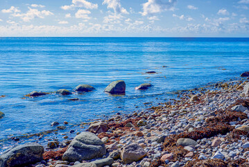 Calm Shoreline Featuring Rounded Stones And Bright Sky. Peaceful Natural Seascape With Smooth Rocks And Clear Blue Waters