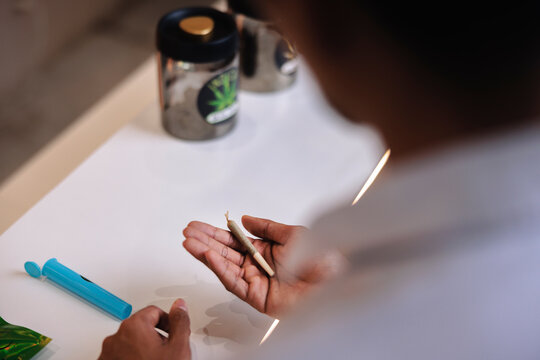 Person holding a cannabis joint with storage containers nearby.