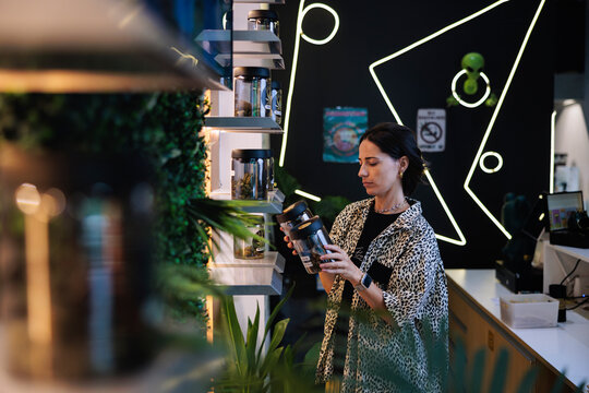 Woman examines cannabis jars in a modern dispensary.