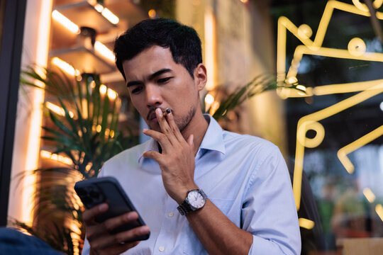 Man smokes while using phone in a cafe.