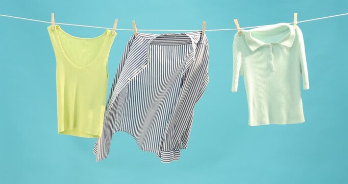 Different clothes drying while hanging on clothesline against light blue background