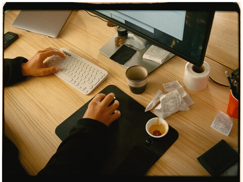 Anonymous person working on a computer at a messy desk